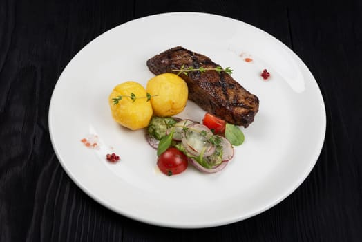 Grilled beef skirt steak meat with potato and vegetables on white plate on wooden black background
