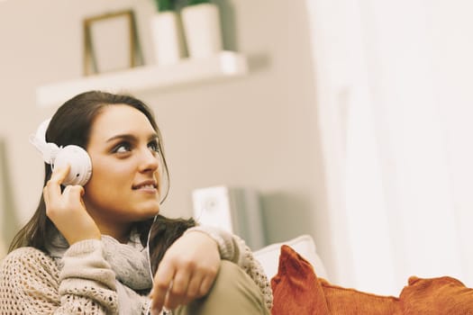 Living room, A young woman is wearing headphones and listening to music while relaxing on her sofa at home