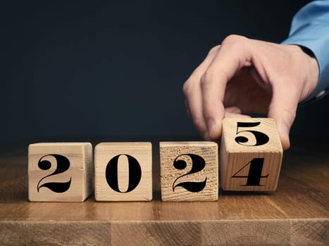A businessman turns a wooden cube from 2024 to 2025, New Years concept