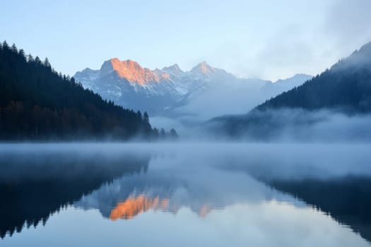 Tranquil alpine lake surrounded by fog-shrouded forests and snow-capped mountain peaks at dawn.