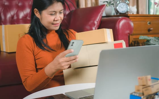 Asia women working business SME online at home her checking order from smartphone  for customer and online delivery for ready packing, Checking orders from customers with digital laptop.