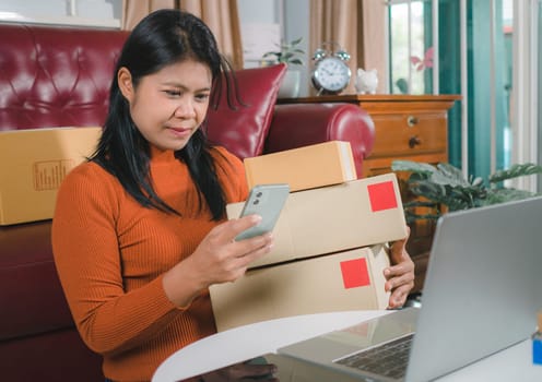 Asia women working business SME online at home her checking order from smartphone  for customer and online delivery for ready packing, Checking orders from customers with digital laptop.