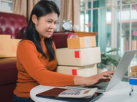 Asia women working business SME online at home her checking order from laptop for customer and online delivery for ready packing, Checking orders from customers with digital laptop, Small business.
