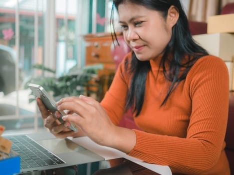 Asia women working business SME online at home her checking order from smartphone  for customer and online delivery for ready packing, Checking orders from customers with digital laptop.