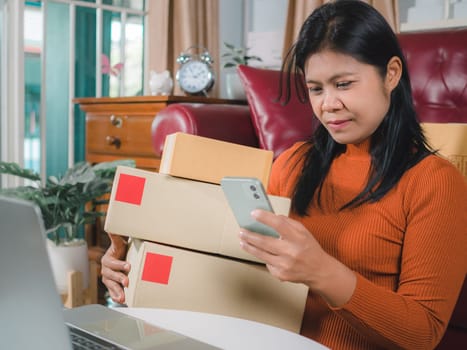 Asia women working business SME online at home her checking order from smartphone  for customer and online delivery for ready packing, Checking orders from customers with digital laptop.