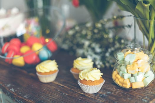 Bright macaroons and cupcakes on a wooden table. Indoors natural light shot with small depth of field