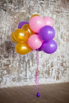 Bright balloons bunch against a textured wall. Copy space