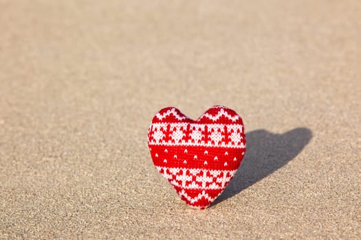 red knitted heart on sea sand. valentine's symbol