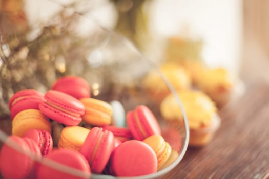 Bright macaroons and cupcakes on a wooden table. Indoors natural light shot with small depth of field