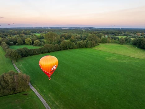 DE LUTTE, NETHERLANDS - AUGUST 21, 2024: Orange hot air balloon searching for a landing spot in a rural landscape