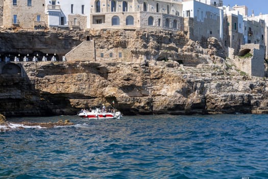 Polignano a Mare, Italy, Apulia - May 24, 2024:  Buildings built on cliffs, view from the sea of ​​picturesque rocks and caves.Terrace of the world famous restaurant Grotta Palazzese in the rock