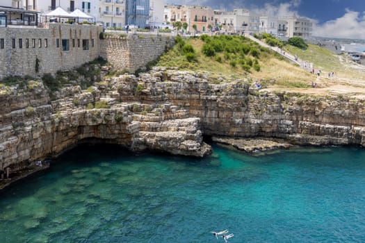 Polignano a Mare, Italy, Apulia - May 24, 2024: Lama Monachile beach, located between picturesque cliffs by Adriatic Sea. People swimming in the water near Grotta Piana