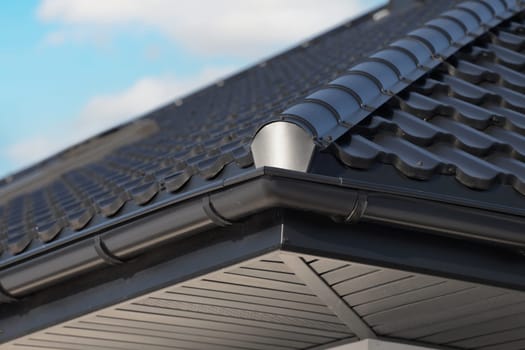 Close-up house roof with steel roofing sheet. Traditional metal shingle tiles. Black modular tile effect roof panel. Profiled metallic corrugated pantile as clay or concrete slate. Building's covering