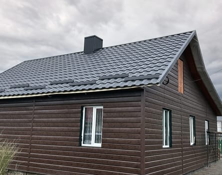 Close-up house roof with steel roofing sheet. Traditional metal shingle tiles. Dark modular tile effect roof panel. Profiled metallic corrugated pantile as clay or concrete slate. Building's covering
