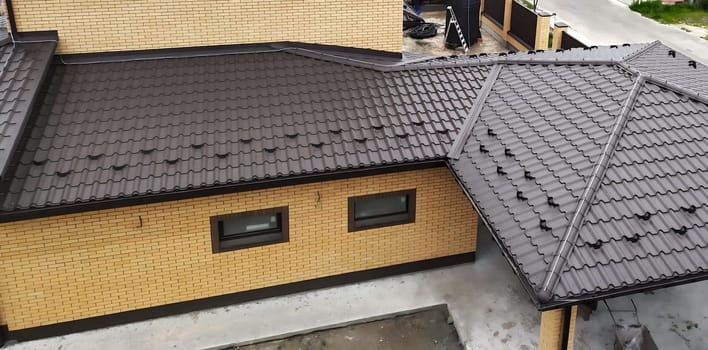 Close-up house roof with steel roofing sheet. Traditional metal shingle tiles. Brown modular tile effect roof panel. Profiled metallic corrugated pantile as clay or concrete slate. Building's covering