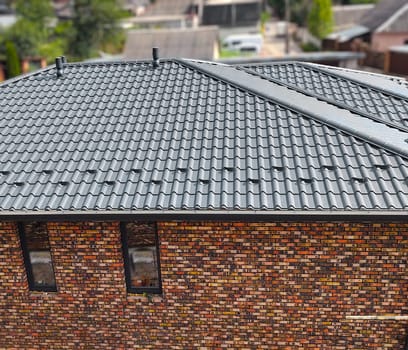 Close-up house roof with steel roofing sheet. Traditional metal shingle tiles. Gray modular tile effect roof panel. Profiled metallic corrugated pantile as clay or concrete slate. Building's covering