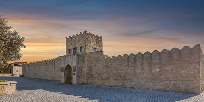 External facade of the Ateshgah Fire Temple in Baku, Azerbaijan, a historic Zoroastrian temple. The stone structure features a stone fence, an arched doorway and a tower with door and small windows