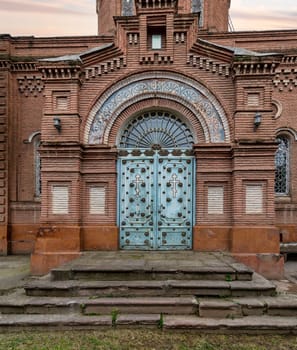 A stunning view of the entrance of Alexander Nevsky Church showcases decorated blue metal door, and intricate red bricks architecture in Ganja, Azerbaijan