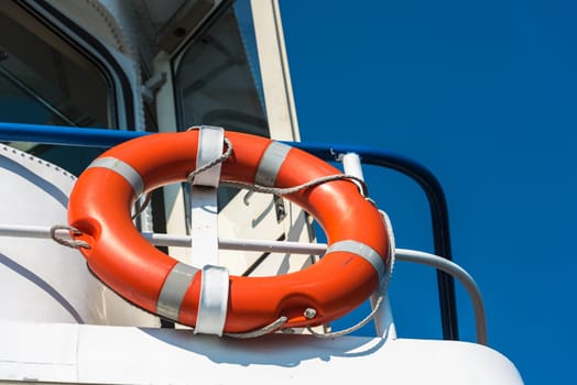Bright orange lifebuoy on a white yacht side. Blue sky background