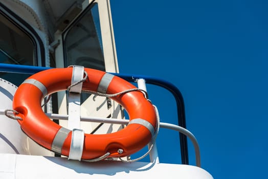 Bright orange lifebuoy on a white yacht side. Blue sky background
