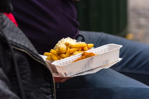 Man holding a street food - french fried and breaded fish in plastic boxes.