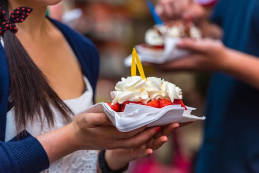 Woman holding typical belgian waffle with red strawberries and whipped cream in the street ready to eat