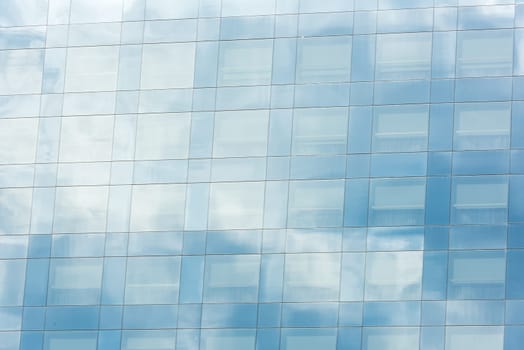 blue sky and clouds reflected in windows of modern office building