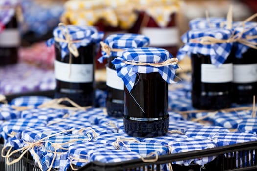 Many preserving jars with dark jam in a market. Horizontal shot