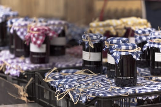 Many preserving jars with dark jam in a market. Horizontal filtered shot