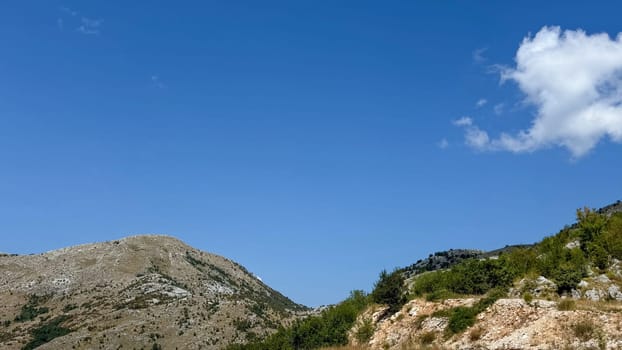 A minimalist landscape featuring a rocky hill with sparse vegetation under a bright, clear blue sky.