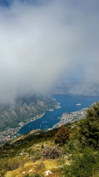 A misty aerial view of a coastal town nestled by a deep blue bay, partially obscured by low-hanging clouds.