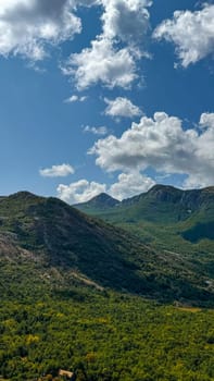 Scenic view of lush green mountains covered with dense foliage against a bright blue sky dotted with fluffy white clouds.Suitable for travel brochures, and environmental awareness campaigns.