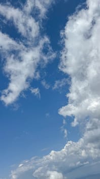 A serene image of a clear blue sky with fluffy white clouds gently floating across the horizon, creating a peaceful and calm atmosphere. copy space.