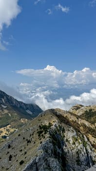 Stunning view of mountain peaks covered with lush vegetation surrounded by floating clouds and clear blue sky.