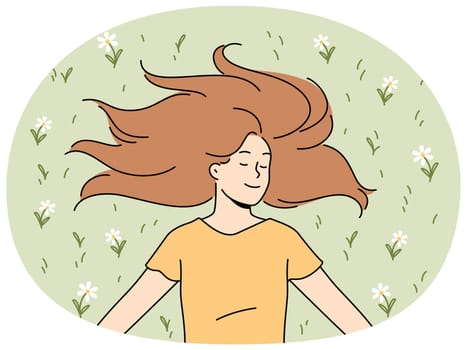 Happy woman with long hair lies on grass in park with eyes closed and smiles rejoicing in sunlight. Positive young woman in casual t-shirt enjoying good summer weather lying on lawn with flowers