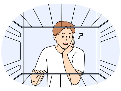 Hungry man sees empty refrigerator and is nervous about lack food due to poverty and financial crisis. Young embarrassed guy looks into refrigerator compartment surprised by lack products on shelves
