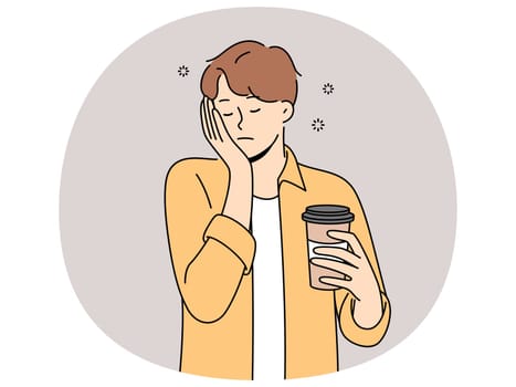 Sleepy man with disposable cup of coffee feels exhausted and lacks strength due to lack of sleep. Guy sleeps on go and tries to cheer up with takeaway coffee with high content of caffeine and taurine