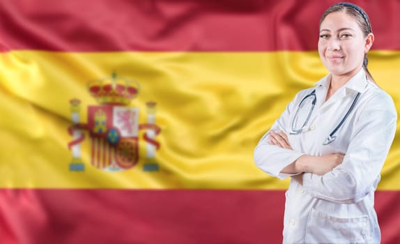 Spanish Health and Care concept. Portrait of female doctor on Spain flag. Doctor with arms crossed on Spanish flag