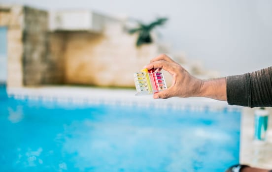 Hand showing tester kit to measure chlorine and ph in swimming pools. Person testing the PH of the swimming pool