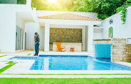 Man cleaning  swimming pool with suction hose. Pool maintenance and cleaning with vacuum hose. Swimming pool cleaning and maintenance service
