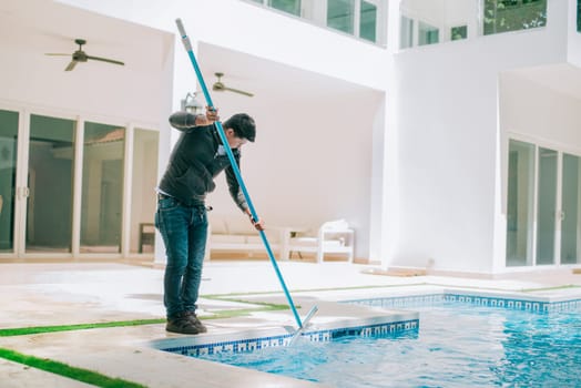 Person cleaning swimming pool with special brush. Maintenance person cleaning home pool with broom