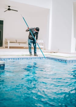Worker cleaning a beautiful homemade swimming pool with skimmer. Maintenance person cleaning a beautiful home swimming pool