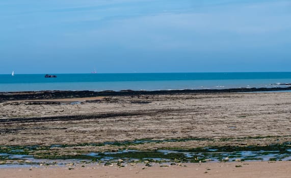 A beach with a boat in the distance and a blue sky. The sky is clear and the water is calm