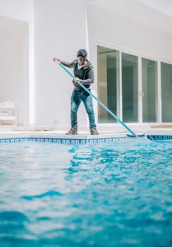 Home pool cleaning with wall brush. Male worker cleaning a home swimming pool with special brush
