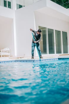 Maintenance person cleaning a beautiful home swimming pool. Worker cleaning a beautiful homemade swimming pool with skimmer