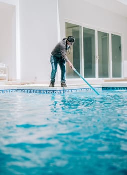 Young man cleaning a swimming pool with suction hose. Swimming pool cleaning and maintenance service