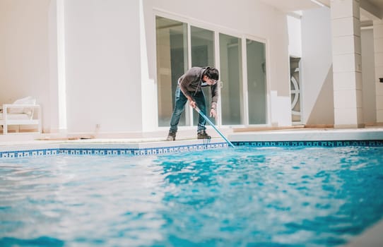 Person cleaning crystal clear pool with special brush. Home pool cleaning with wall brush