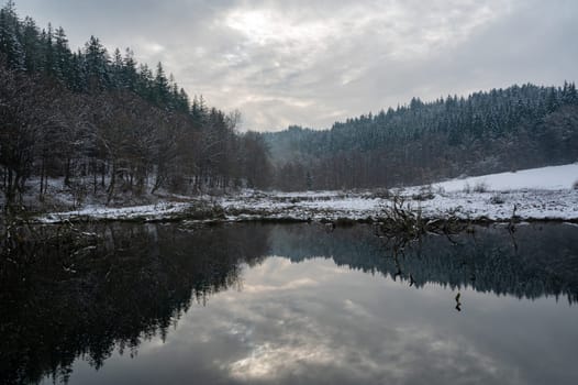 A small lake with forest and reflections in the water, in winter time with snow