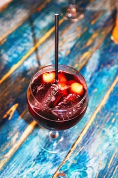 A glass of cold traditional Spanish drink sangria cocktail with fresh assorted fruits and a straw on blurred blue wooden table. Spain, Canary island, Gran Canaria.