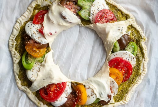 A pizza with a variety of vegetables including tomatoes, peppers, and cheese. The pizza is in the shape of a wreath